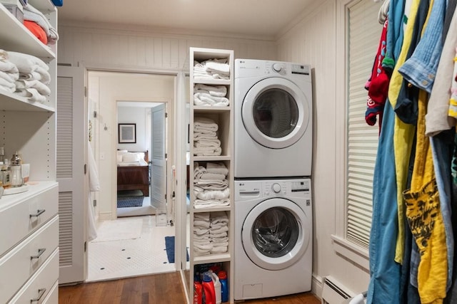 laundry room with stacked washing maching and dryer, wooden walls, dark wood-type flooring, and a baseboard radiator