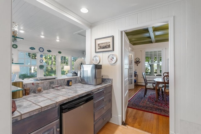 kitchen with light hardwood / wood-style floors, tile counters, beam ceiling, dark brown cabinetry, and stainless steel dishwasher