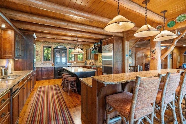 kitchen featuring a center island with sink, wood ceiling, a sink, light wood-style flooring, and stainless steel built in refrigerator