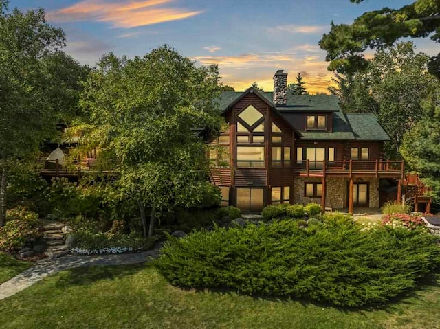 back house at dusk featuring a lawn and a wooden deck