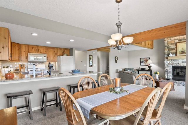 carpeted dining space featuring a chandelier, a textured ceiling, sink, and a stone fireplace