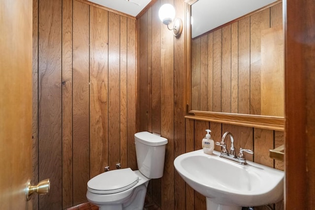 bathroom featuring sink, wooden walls, and toilet