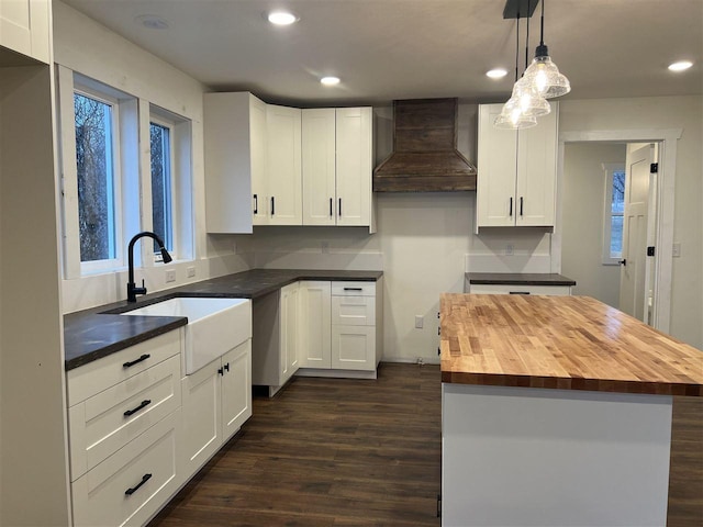 kitchen featuring sink, butcher block countertops, decorative light fixtures, a kitchen island, and custom range hood