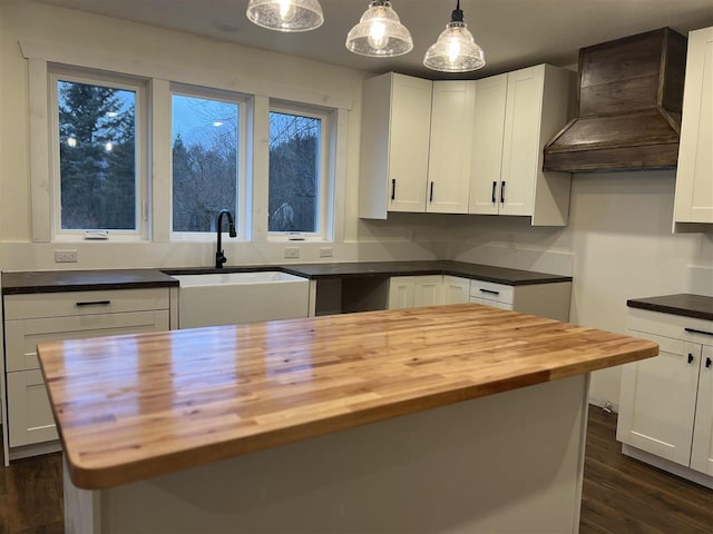 kitchen featuring pendant lighting, wood counters, a center island, sink, and custom range hood