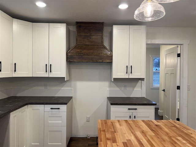 kitchen featuring premium range hood, butcher block counters, white cabinetry, and hanging light fixtures