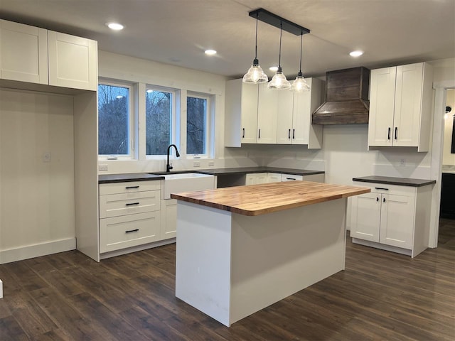 kitchen with custom exhaust hood, a kitchen island, sink, white cabinetry, and hanging light fixtures