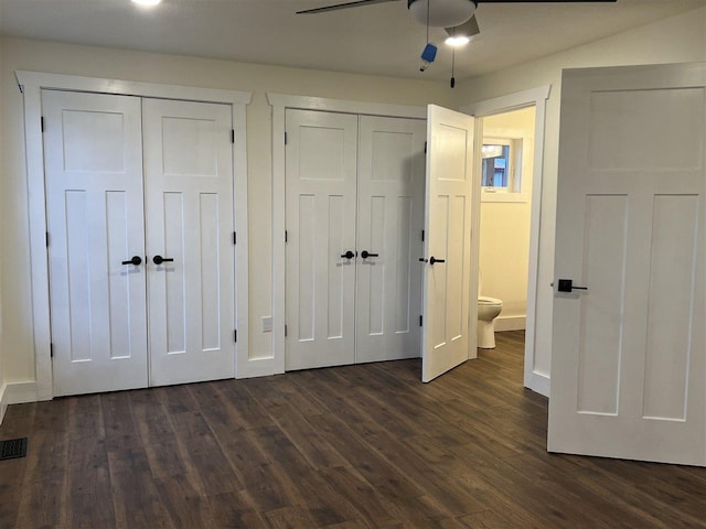 unfurnished bedroom featuring dark wood-type flooring, ceiling fan, and multiple closets