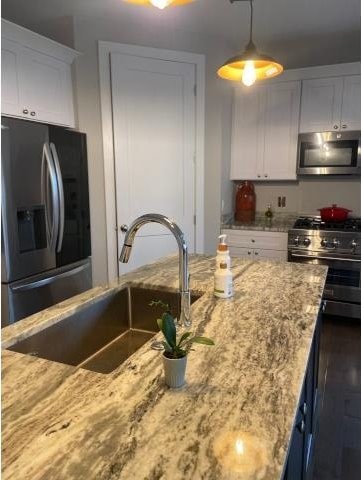 kitchen featuring light stone countertops, sink, hanging light fixtures, white cabinetry, and stainless steel appliances