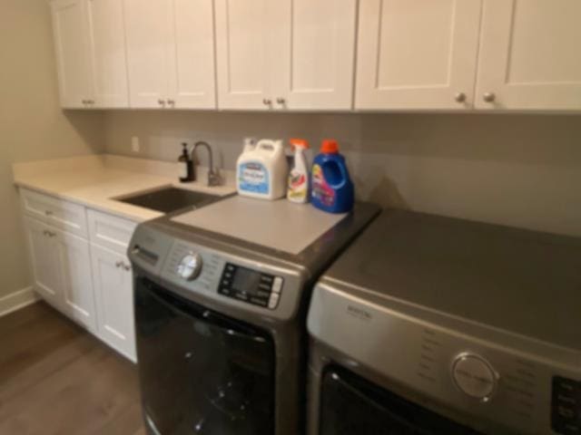 clothes washing area featuring cabinets, sink, washing machine and dryer, and dark hardwood / wood-style flooring