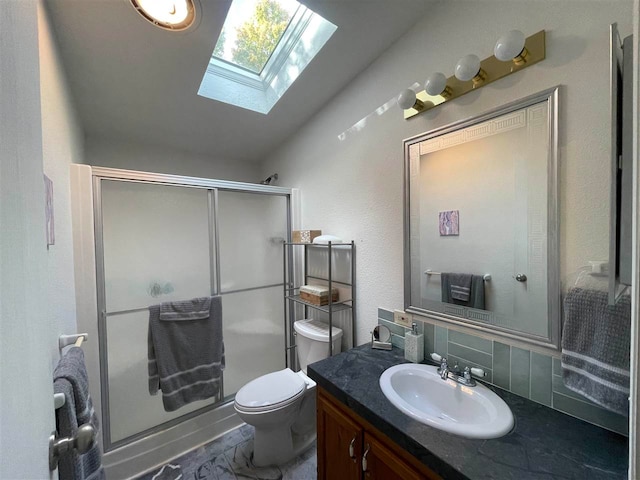 bathroom featuring vanity, a shower with shower door, toilet, vaulted ceiling with skylight, and backsplash