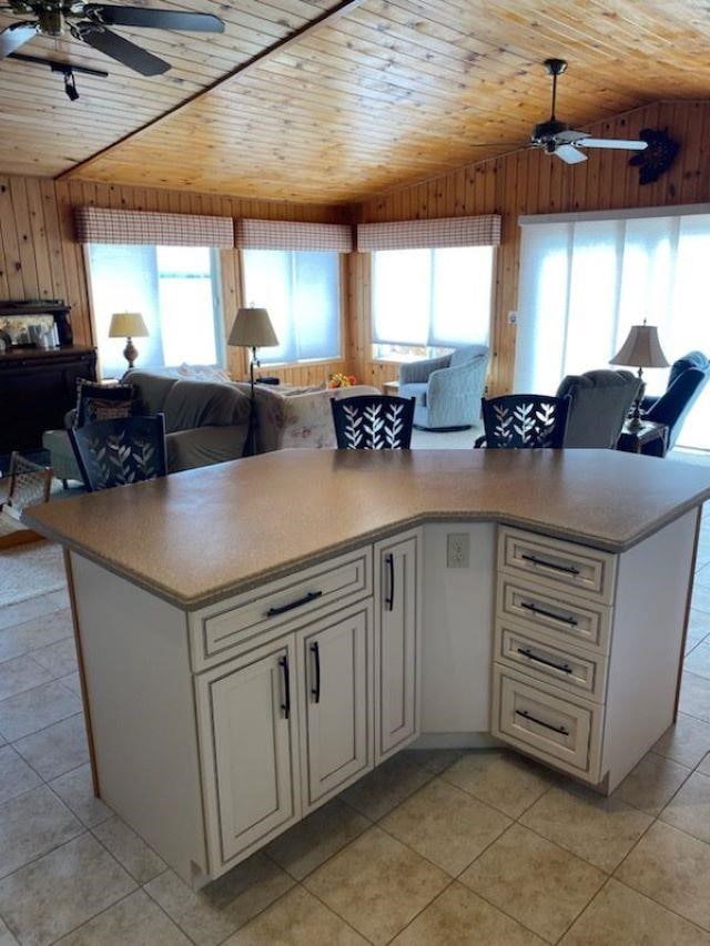 kitchen featuring wood ceiling, ceiling fan, light tile patterned floors, vaulted ceiling, and wood walls