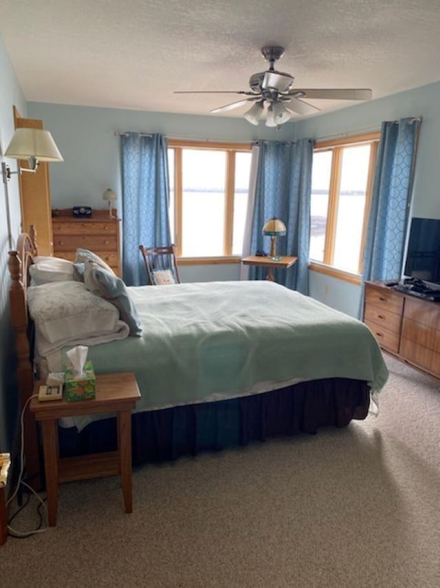 carpeted bedroom with a textured ceiling, multiple windows, and ceiling fan