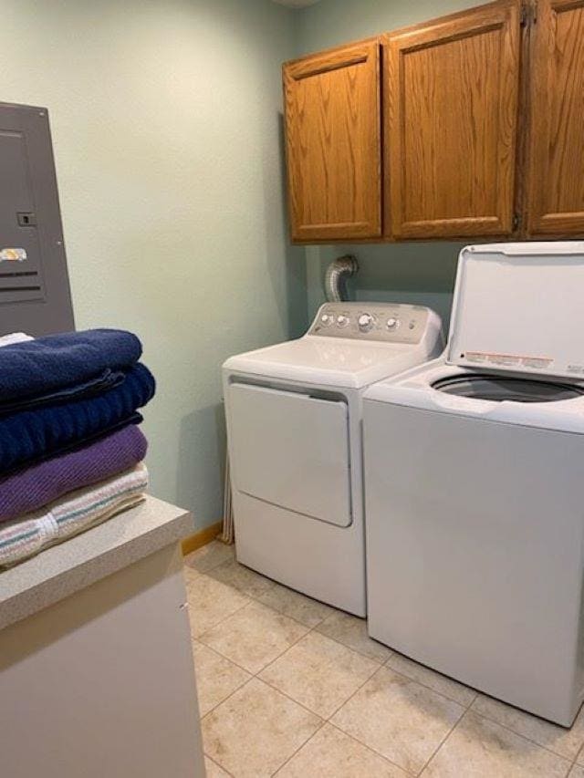 washroom featuring electric panel, washing machine and dryer, light tile patterned floors, and cabinets