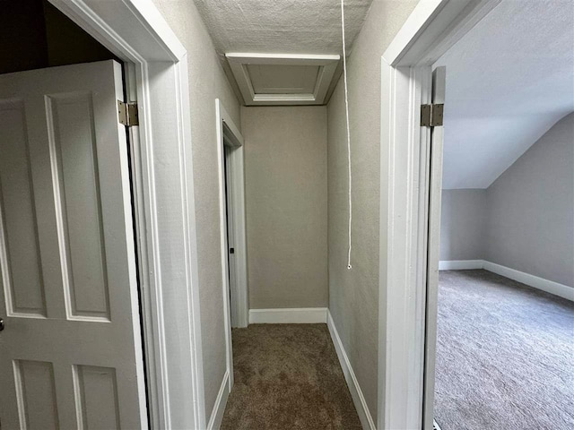 hallway with a textured ceiling, lofted ceiling, and dark colored carpet