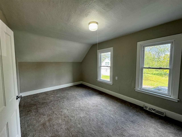 additional living space featuring plenty of natural light, vaulted ceiling, and dark colored carpet