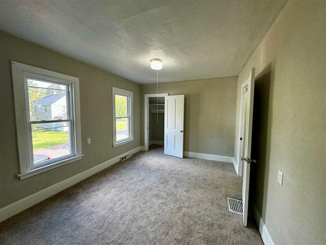 unfurnished bedroom with a spacious closet, a closet, light colored carpet, and a textured ceiling