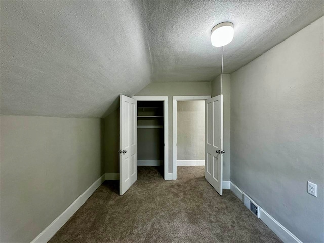 unfurnished bedroom with lofted ceiling, dark colored carpet, and a textured ceiling