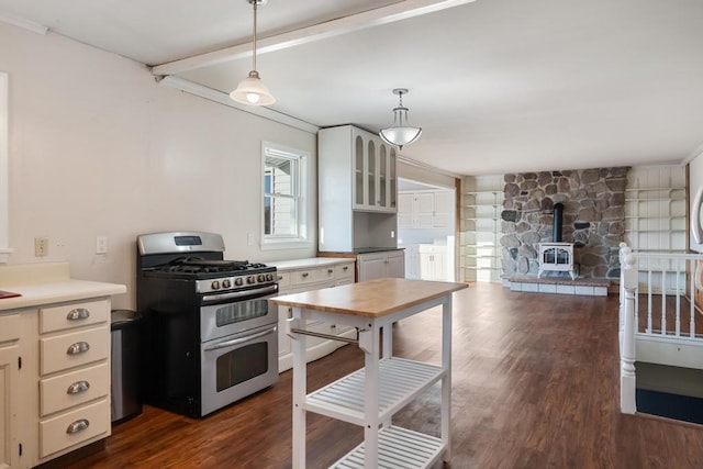 kitchen featuring dark hardwood / wood-style flooring, white cabinetry, gas range, pendant lighting, and a wood stove