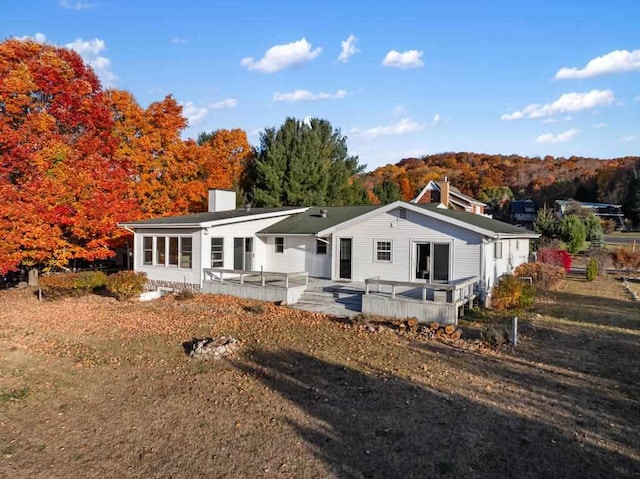 rear view of property featuring a lawn, a chimney, and a wooden deck