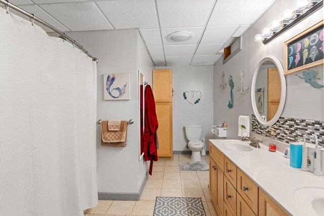 bathroom featuring tile patterned floors, toilet, a drop ceiling, vanity, and tasteful backsplash