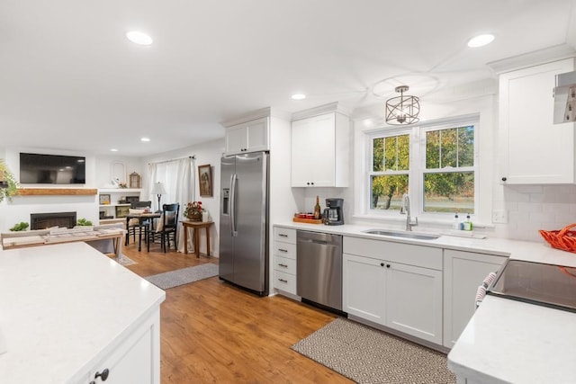 kitchen featuring white cabinets, sink, light hardwood / wood-style floors, decorative light fixtures, and stainless steel appliances