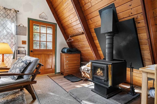 interior space with wood ceiling, wood-type flooring, vaulted ceiling, wood walls, and a wood stove