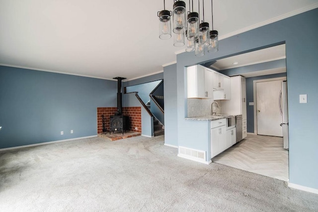 1185 Hideaway Valley Dr Unit 5, Harbor Springs, MI 49740 - unfurnished living room with ornamental molding, baseboards, a sink, a wood stove, and light colored carpet
