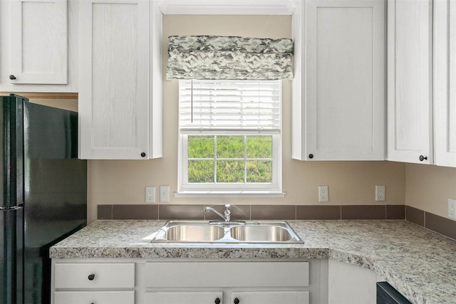 kitchen featuring sink, black refrigerator, and white cabinets