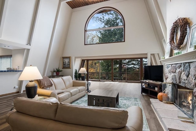 living room with a high ceiling, light wood-type flooring, a stone fireplace, and a healthy amount of sunlight