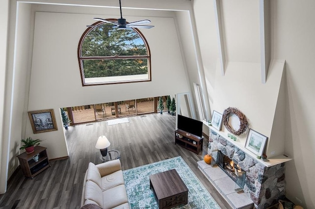 living room featuring hardwood / wood-style flooring, ceiling fan, and a stone fireplace