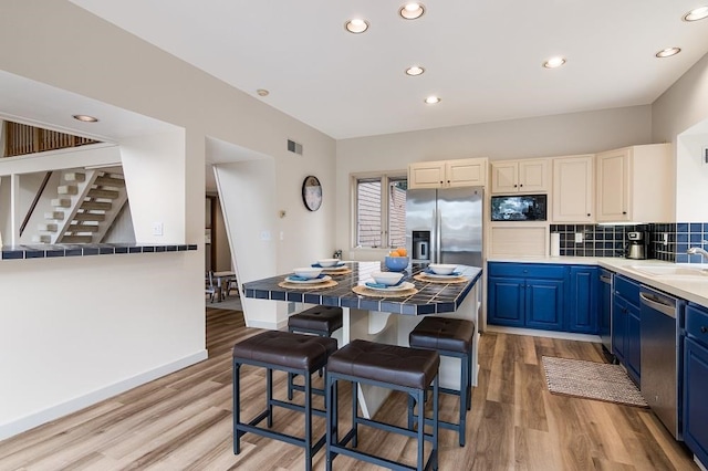 kitchen with stainless steel appliances, light wood-type flooring, blue cabinetry, sink, and a kitchen breakfast bar