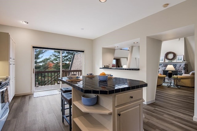 kitchen featuring stainless steel range, tile countertops, a breakfast bar area, and dark wood-type flooring