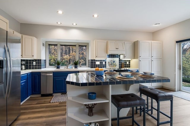 kitchen featuring tile countertops, stainless steel refrigerator with ice dispenser, blue cabinetry, a kitchen island, and light wood-type flooring