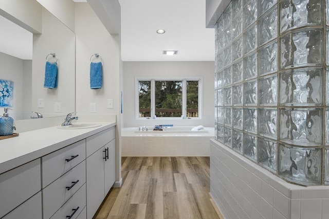 bathroom with tiled bath, wood-type flooring, and vanity