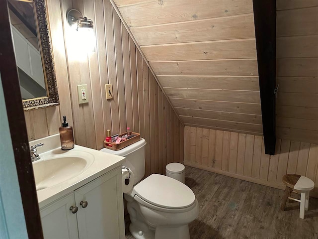 bathroom with vanity, wooden walls, hardwood / wood-style floors, vaulted ceiling, and toilet