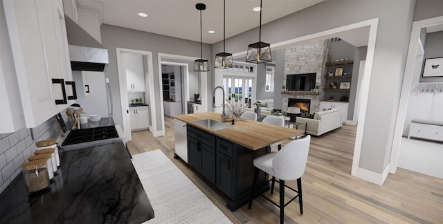 kitchen featuring a center island with sink, sink, hanging light fixtures, a stone fireplace, and range hood