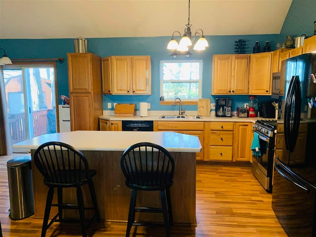 kitchen featuring sink, light hardwood / wood-style floors, vaulted ceiling, decorative light fixtures, and black appliances