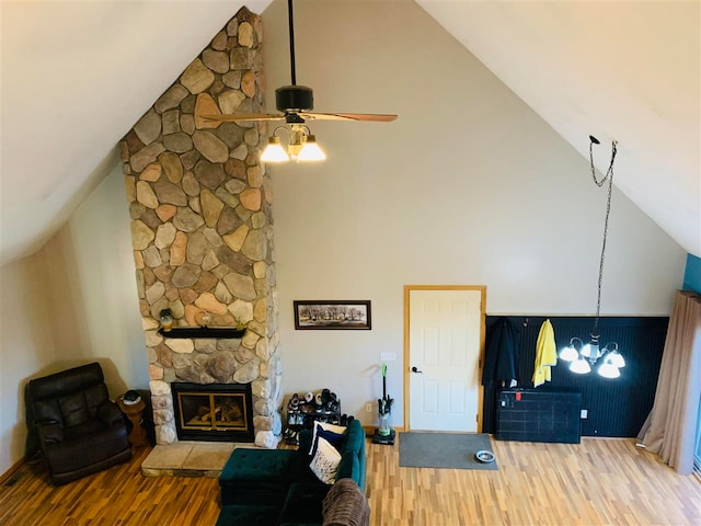 living room featuring ceiling fan with notable chandelier, hardwood / wood-style flooring, a stone fireplace, and high vaulted ceiling