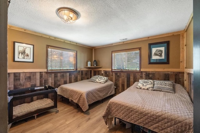 bedroom with light wood-type flooring, a textured ceiling, wooden walls, and ornamental molding