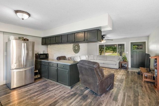 kitchen featuring a textured ceiling, ceiling fan, dark wood-type flooring, and stainless steel refrigerator