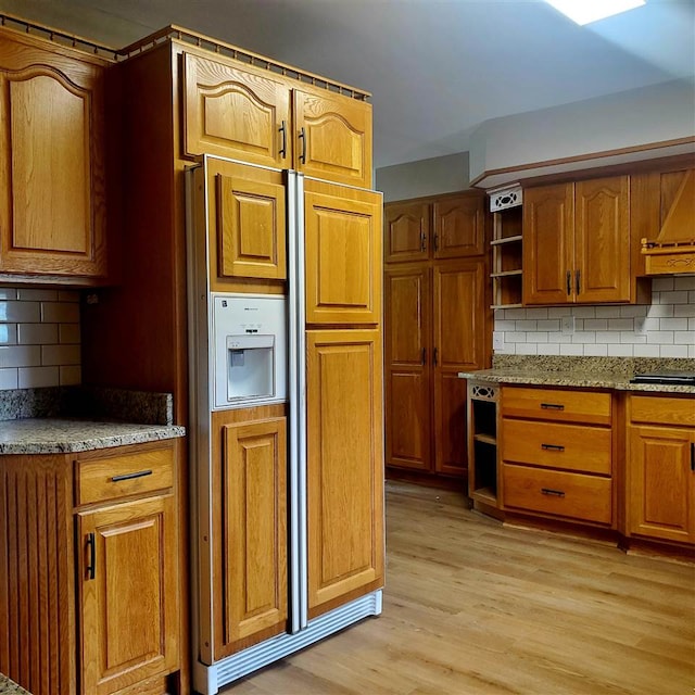 kitchen featuring paneled built in refrigerator, decorative backsplash, light wood-type flooring, and light stone countertops