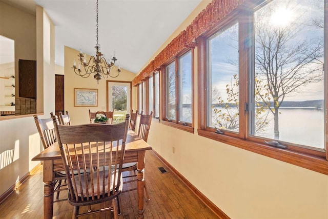 dining area with hardwood / wood-style floors, a water view, vaulted ceiling, and a notable chandelier