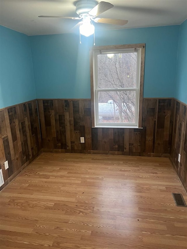 spare room featuring wooden walls, light hardwood / wood-style flooring, and ceiling fan