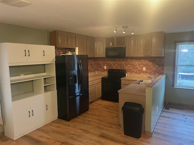 kitchen with sink, tasteful backsplash, kitchen peninsula, light hardwood / wood-style floors, and black appliances