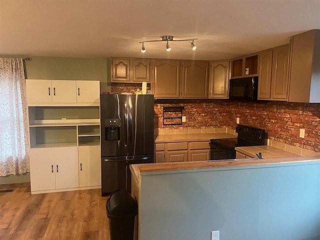 kitchen featuring tile countertops, backsplash, black appliances, light wood-type flooring, and kitchen peninsula