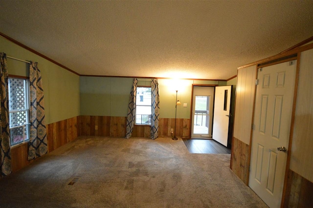 unfurnished room featuring carpet, a textured ceiling, crown molding, and wooden walls