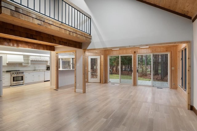 unfurnished living room featuring light hardwood / wood-style floors, high vaulted ceiling, wood ceiling, and wood walls