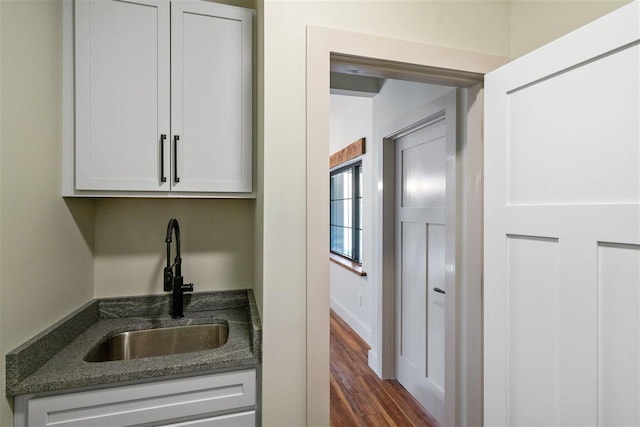 kitchen with dark hardwood / wood-style flooring, white cabinetry, dark stone counters, and sink