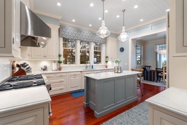 kitchen featuring dark hardwood / wood-style flooring, light stone counters, wall chimney range hood, decorative light fixtures, and a kitchen island