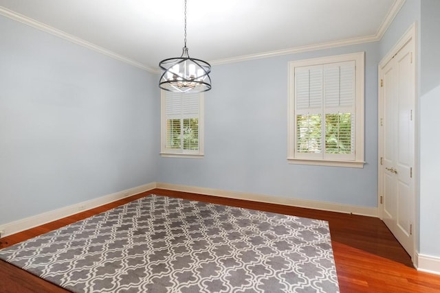 empty room with hardwood / wood-style flooring, crown molding, and a notable chandelier